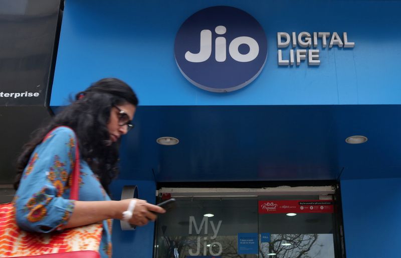 © Reuters. Una mujer revisa su teléfono móvil cuando pasa por delante de una tienda de móviles de la unidad de telecomunicaciones Jio de Reliance Industries, en Bombay, India