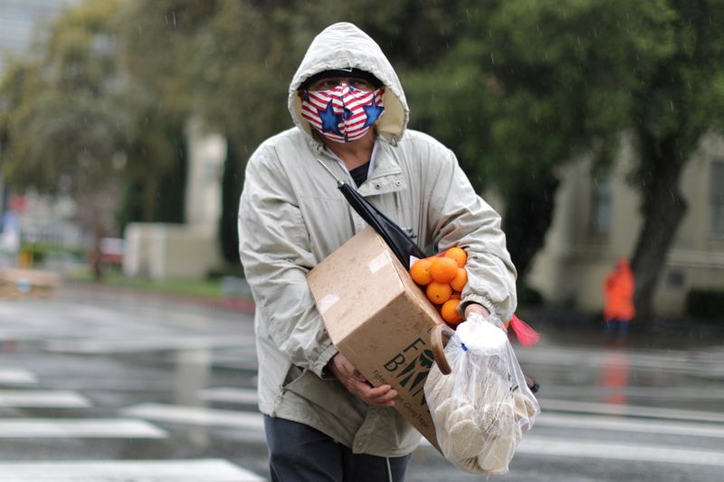© Reuters. FOTO DE ARCHIVO: Un hombre lleva alimentos frescos bajo la lluvia en un sorteo del Banco de Alimentos Regional de Los Ángeles de 2,000 cajas de comestibles, mientras continúa la propagación de la enfermedad por coronavirus (COVID-19), en Los Ángeles