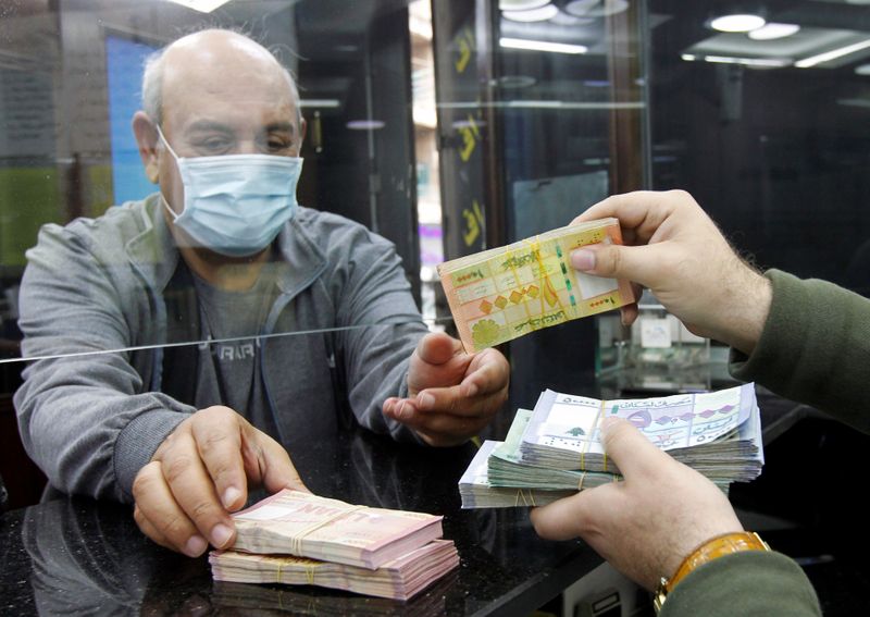 © Reuters. Un hombre con una máscara facial toma billetes de libra libanesa en una tienda de cambio de moneda en Beirut