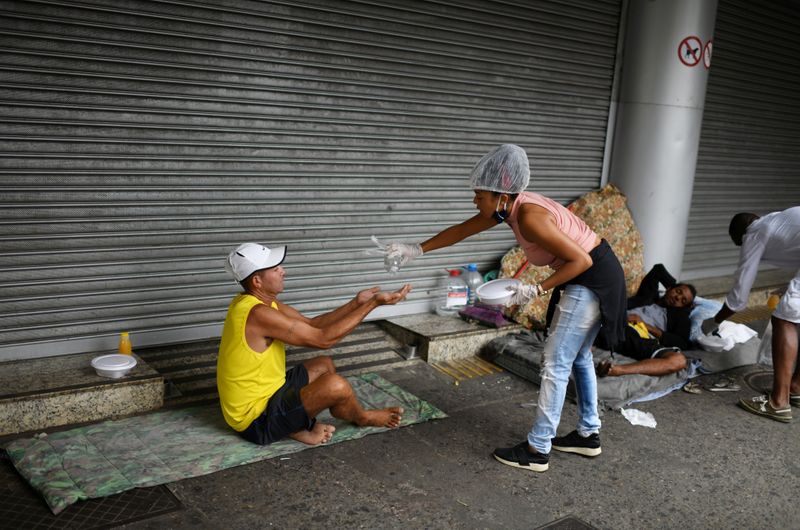 © Reuters. Voluntária despeja álcool gel na mão de homem durante ação de entrega de comida para pessoas em situação de rua no Rio de Janeiro