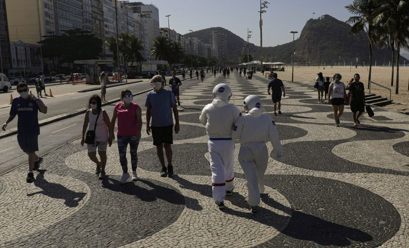 &copy; Reuters. Tercio Galdino, de 66 años, y su esposa Aliceia, de 65 años, usan &quot;trajes espaciales&quot; protectores mientras caminan por la acera de la playa de Copacabana, Río de Janeiro