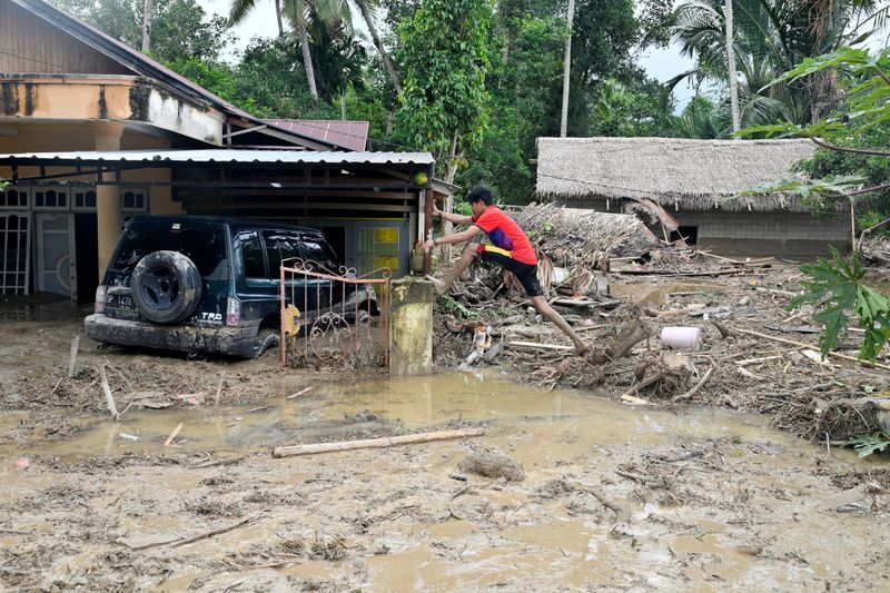 &copy; Reuters. A man steps over debris near a house submerged in mud after flash floods swept through Radda village, as several people were killed and dozens remain missing in North Luwu, Sulawesi