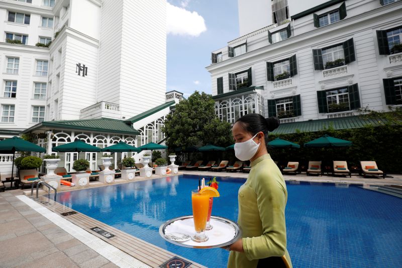 &copy; Reuters. FILE PHOTO: A woman wearing a protective mask carries glasses of fruit juice by the swimming pool of the Sofitel Legend Metropole hotel in Hanoi