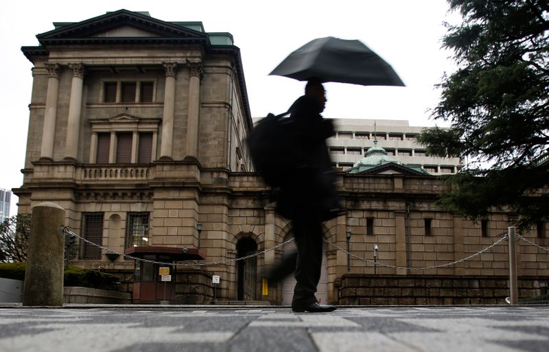 &copy; Reuters. A pedestrian holding an umbrella to take shelter from rain and hail walks past the Bank of Japan headquarters building in Tokyo