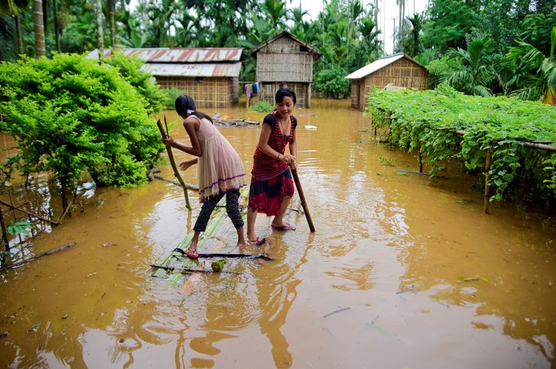 &copy; Reuters. Girls row a makeshift raft past submerged houses at a flood-affected village in Karbi Anglong district