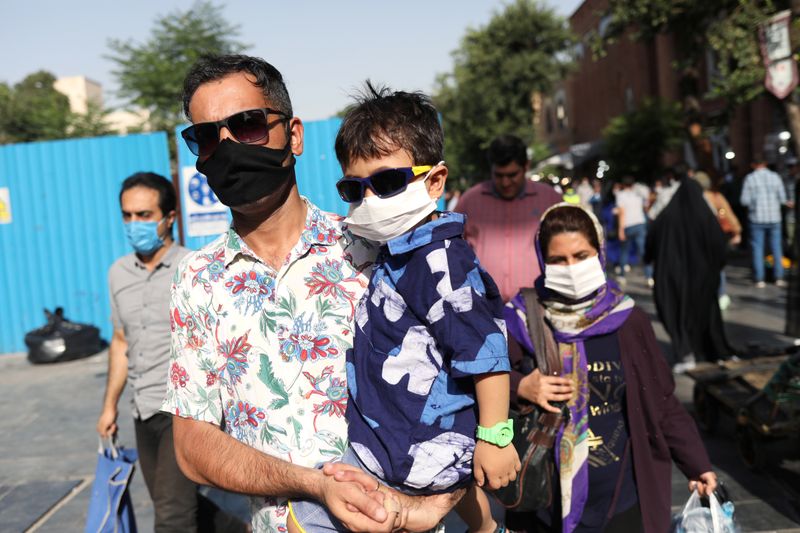 &copy; Reuters. An Iranian man and his son wearing a protective face mask walks in a street, following the outbreak of the coronavirus disease (COVID-19), in Tehran