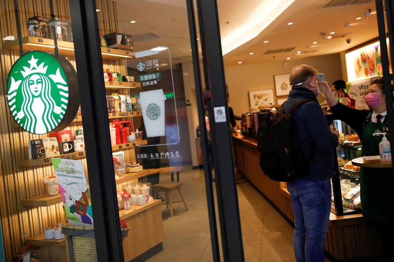 &copy; Reuters. Worker uses a thermometer to check the temperature of a customer as he enters a Starbucks shop as the country is hit by an outbreak of the new coronavirus, in Beijing