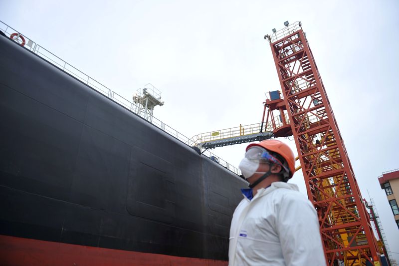 &copy; Reuters. Dock worker wearing a face mask looks at an oil tanker unloading crude oil at a port in Qingdao