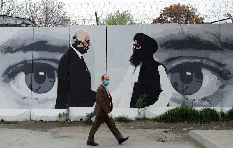 &copy; Reuters. FILE PHOTO: An Afghan man wearing a protective face mask walks past a wall painted with photo of Zalmay Khalilzad, U.S. envoy for peace in Afghanistan, and Mullah Abdul Ghani Baradar, the leader of the Taliban delegation, in Kabul