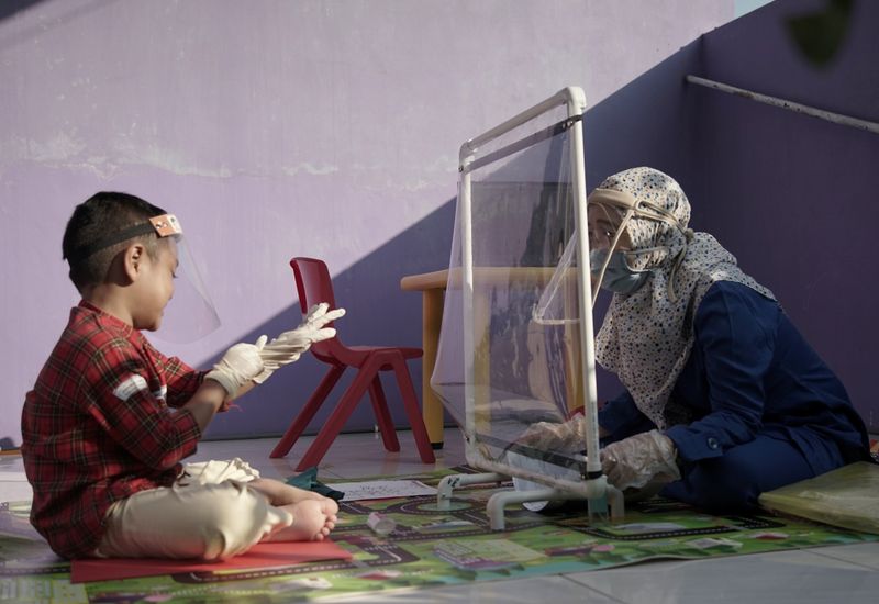 &copy; Reuters. A teacher wearing a face shield and protective mask talks with her pupil through a plastic barrier as she visits her pupil at their house to evaluate their online class-session amid the coronavirus disease (COVID-19) outbreak in Semarang