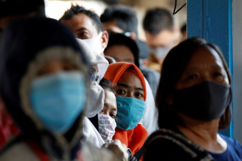 &copy; Reuters. Pessoas usam máscaras em fila para pegar ônibus em Jacarta