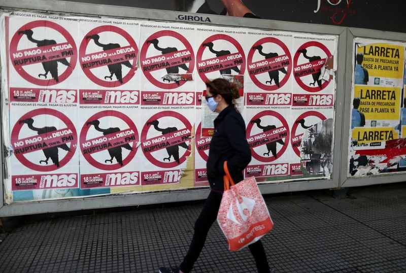 &copy; Reuters. FILE PHOTO: A pedestrian wearing a protective face mask walks past posters on the street that read &quot;No to the payment of the debt. Break with the IMF&quot;, in Buenos Aires