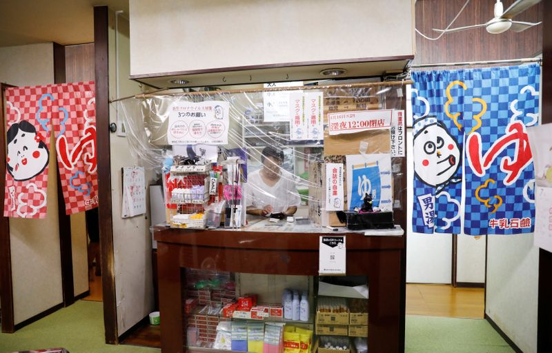 &copy; Reuters. Iwasaki, wife of the owner of public bathhouse works behind a plastic curtain in Tokyo