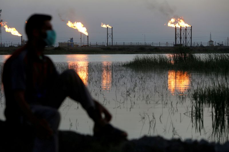 &copy; Reuters. FILE PHOTO: Flames emerge from flare stacks at Nahr Bin Umar oil field, as a man is seen wearing a protective face mask , following the outbreak of the coronavirus, north of Basra