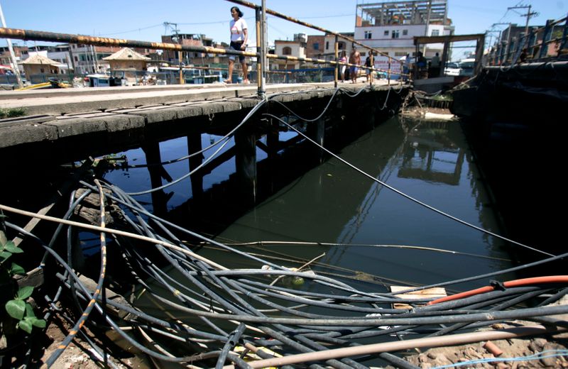 &copy; Reuters. Residente de favela Nova Holanda caminha por mangueiras usadas para puxar água de rio poluído em Macaé