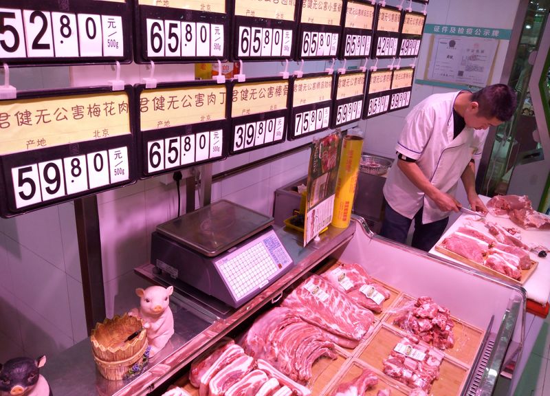 &copy; Reuters. FILE PHOTO: An employee works next to signs showing pork prices at a market in Beijing