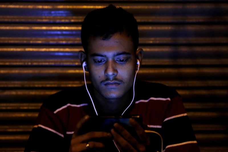 &copy; Reuters. FILE PHOTO: A man watches a movie on his phone as he waits for the bank to open to exchange his old high-denomination banknotes in Delhi