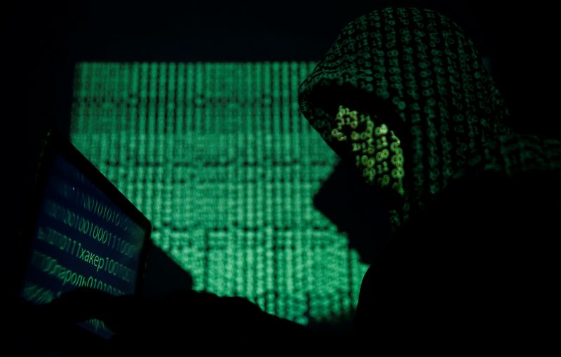 © Reuters. Hooded man holds a laptop computer as cyber code is projected on him in this illustration picture