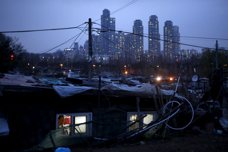 © Reuters. FILE PHOTO: A man looks out from his shack as a luxury high-rise apartment complex is seen in the background at Guryong village in Seoul