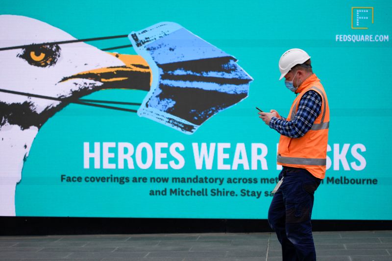 &copy; Reuters. FILE PHOTO: An essential worker wearing a face mask walks past a &apos;Heroes Wear Masks&apos; sign in Melbourne, the first city in Australia to enforce mask-wearing to curb a resurgence of COVID-19