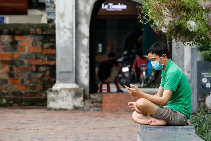 &copy; Reuters. A man wearing a protective face mask looks at a smart phone amid the coronavirus disease (COVID-19) outbreak, at the temple of literature in Hanoi