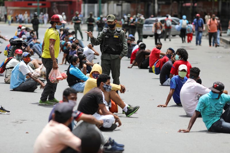 &copy; Reuters. Foto del miércoles de un miembro de la Guardia nacional de Venezuela entre un grupo de personas sentadas bajo el sol por no cumplir con las normas de salud por la pandemia de coronavirus en una calle en Caracas