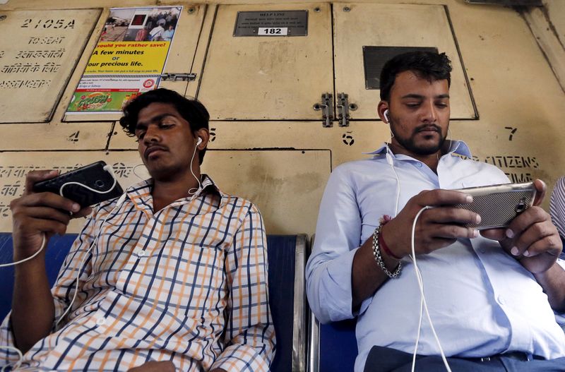 &copy; Reuters. FILE PHOTO: Commuters watch videos on their mobile phones as they travel in a suburban train in Mumbai