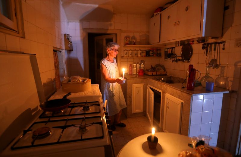 &copy; Reuters. FILE PHOTO: Samira Hanna,70, walks in her kitchen as she holds a candle due to a power cut, in Beirut