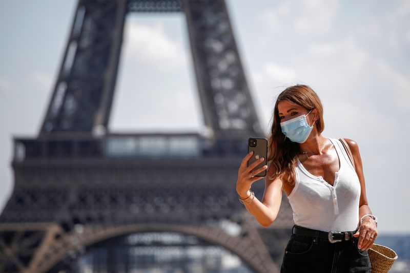 &copy; Reuters. Mulher com máscara tira foto em frente à Torre Eiffel