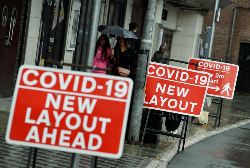 © Reuters. Consumidores passam por placas alertando para distanciamento social em Londres