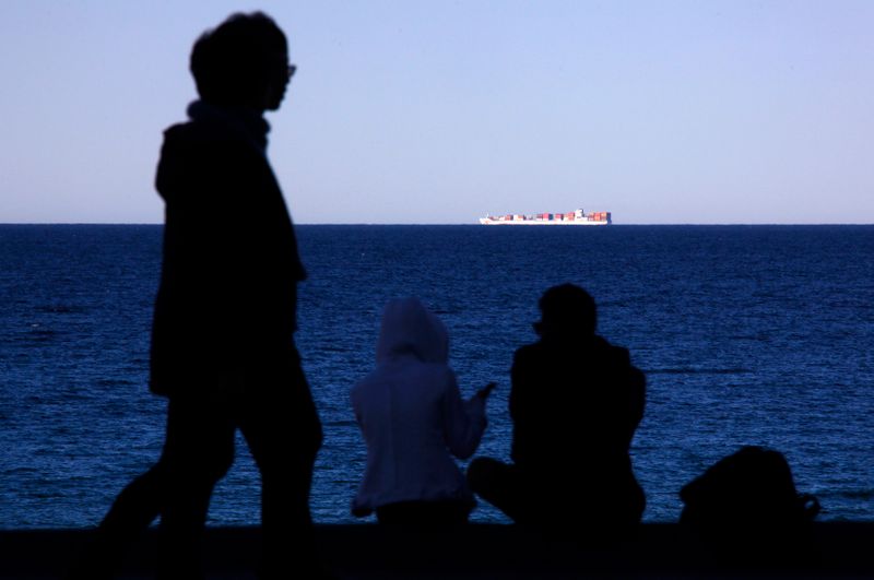 &copy; Reuters. People sit and walk along a footpath as a container ship sails on the horizon at Sydney&apos;s Manly Beach