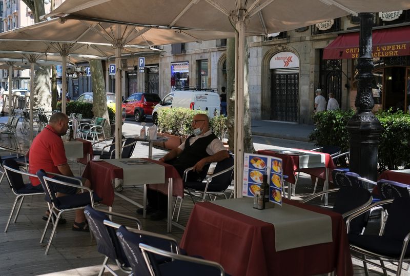 &copy; Reuters. Un camarero se sienta en la terraza en la que trabaja a la espera de clientes, después de que el Gobierno de Cataluña anunciase restricciones para contener la propagación del virus