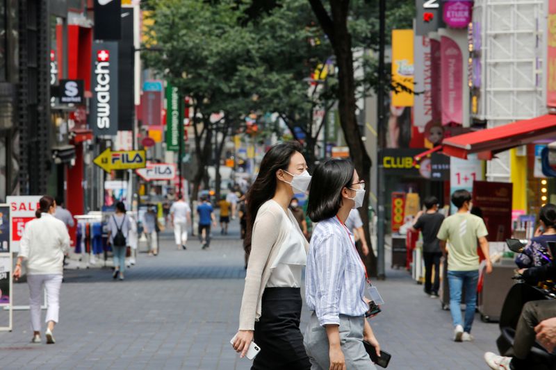 &copy; Reuters. Mulheres com máscara de proteção contra Covid-19 caminham por distrito de compras em Seul