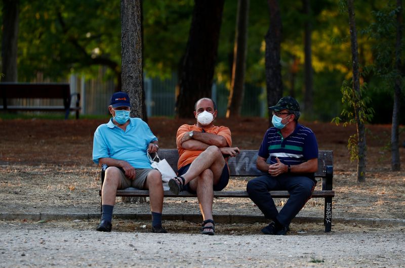 &copy; Reuters. Tres hombres con mascarillas sentados en un banco en el parque de Las Cruces en Madrid, España