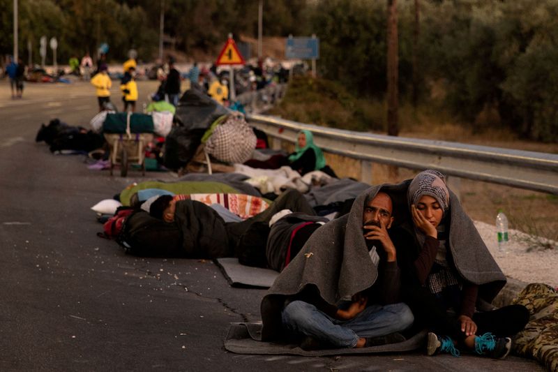 &copy; Reuters. FILE PHOTO: Couple sits covered with a blanket as refugees and migrants camp on a road following a fire at the Moria camp on the island of Lesbos