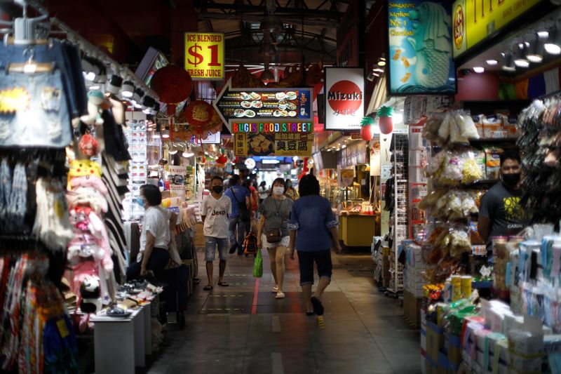 &copy; Reuters. FILE PHOTO: People wearing protective face masks walk past shops, in Singapore