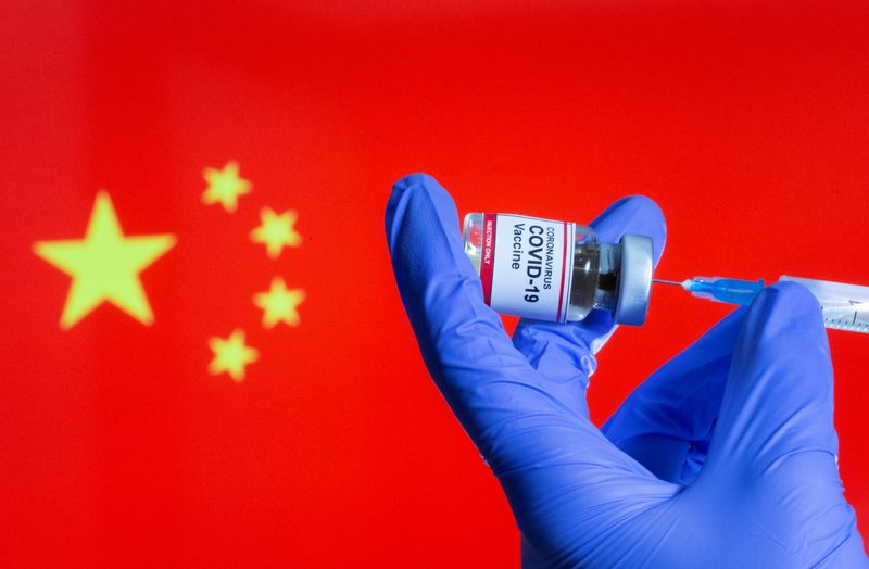 &copy; Reuters. A woman holds a small bottle labeled with a &quot;Coronavirus COVID-19 Vaccine&quot; sticker and a medical syringe in front of displayed China flag in this illustration