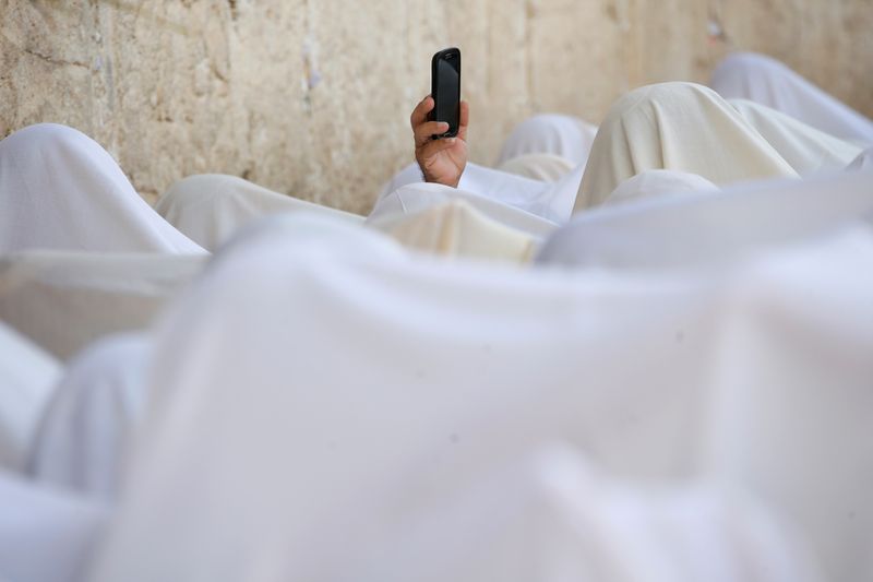 © Reuters. FILE PHOTO: A Jewish worshipper uses his mobile phone to record worshippers who are covered in prayer shawls as they recite the priestly blessing at the Western Wall in Jerusalem's Old City during the Jewish holiday of Sukkot