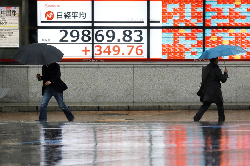 &copy; Reuters. Men holding umbrellas walk in front of an electric board showing Nikkei index at a brokerage in Tokyo