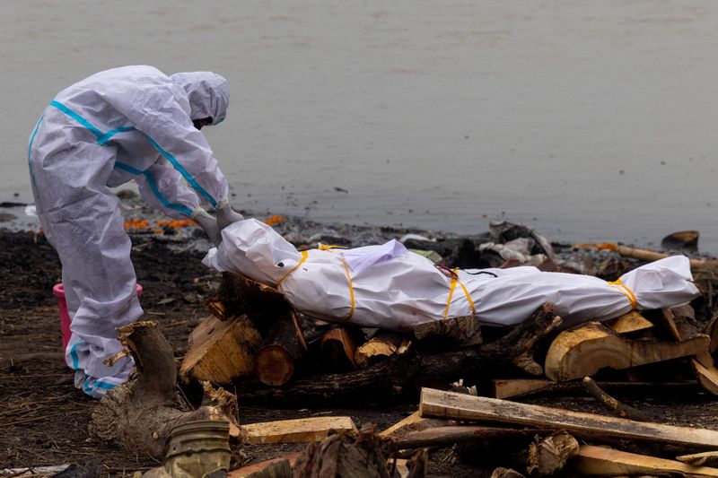 &copy; Reuters. رجل يرتدي ملابس واقية بجانب جثة أحد أقاربه الذي توفي بسبب إصابته بفيروس كورونا قبل حرق جثته على ضفاف نهر الجانج في ولاية أوتار براديش بشمال 