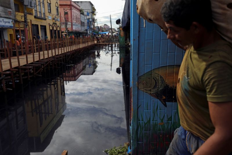 &copy; Reuters. A man carries a bag as he walks over wooden walkways installed by the city hall over a street flooded by waters from the Negro river in downtown of Manaus, in Amazonas State, Brazil May 17, 2021. REUTERS/Bruno Kelly