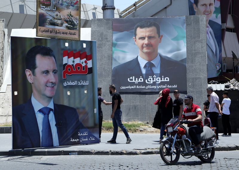 &copy; Reuters. أشخاص يسيرون قرب ملصقات دعائية للأسد في دمشق يوم 22 مايو ايار 2021. تصوير رويترز.