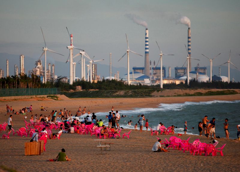 &copy; Reuters. FOTO DE ARCHIVO. Molinos de viento y una central eléctrica se ven a lo lejos mientras los bañistas ven la puesta de sol en la ciudad de Dongfang, en el lado occidental de la provincia insular china de Hainan. 18 de junio de 2014. REUTERS/John Ruwitch