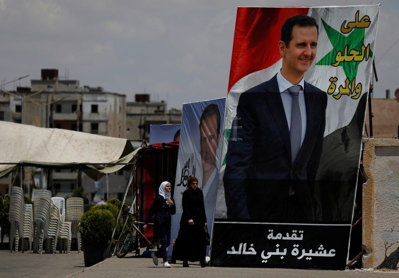 &copy; Reuters. امرأتان تمران عبر لافتة انتخابية للرئيس السوري بشار الأسد في حمص يوم 23 مايو آيار 2023. تصوير: عمر صناديقي - رويترز.