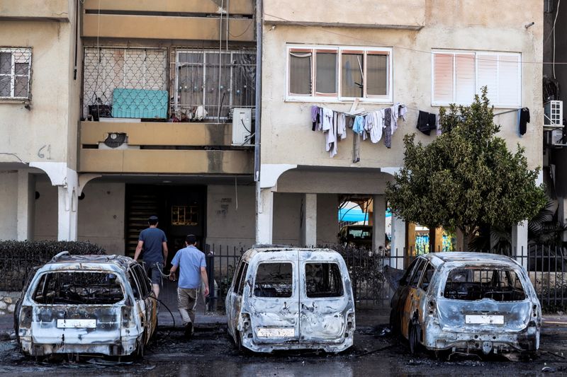&copy; Reuters. FILE PHOTO: People walk next to burnt vehicles as they enter a building after violent confrontations in the city of Lod, Israel, between Israeli Arab demonstrators and police,  amid high tensions over hostilities between Israel and Gaza militants and tens